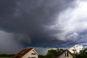 Big ominous thunderclouds over roofs and green trees