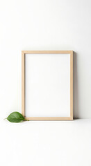 Empty Natural Wood Frame Leaning on White with a Green Leaf