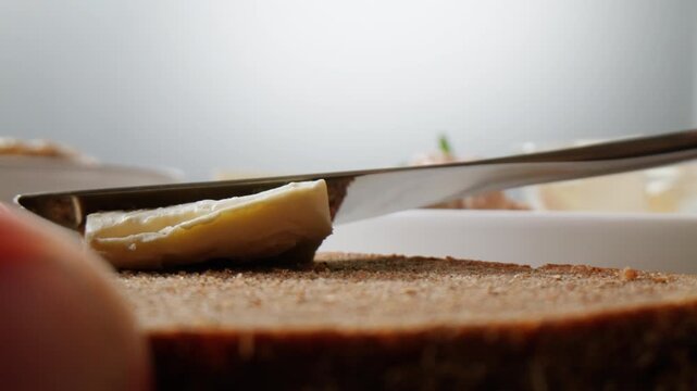 Young woman spreading nut butter on rye black bread toast in kitchen, closeup