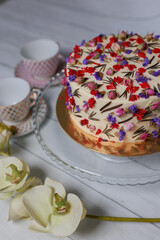 An elegant white cake with dried flowers all over, with a close-up of the floral details. The cake sits on a glass stand.