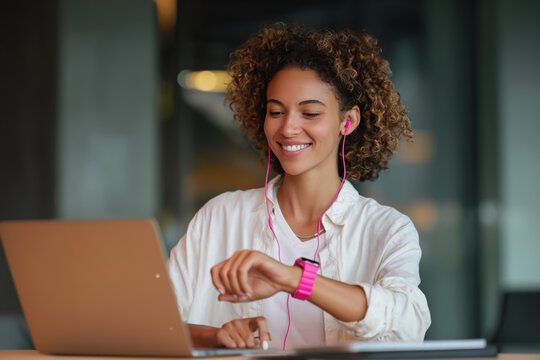 Young woman smiling while checking her smartwatch and working on a laptop