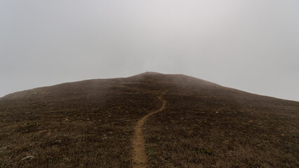 Solitary Hiker on a Foggy Coastal Hill Trail