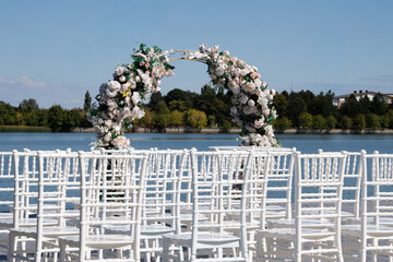 Wooden pontoon decorated with a floral arch, prepared for a romantic outdoor religious wedding ceremony by the water