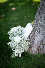 Bridal bouquet made of small white flowers placed on green grass near a tree, symbolising purity, romance and natural elegance