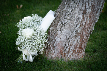 Bridal bouquet made of small white flowers placed on green grass near a tree, symbolising purity, romance and natural elegance
