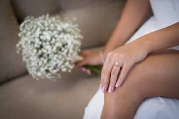 Bride holding a delicate wedding bouquet with small white flowers, showcasing her elegant engagement ring on the hand.