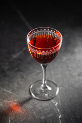 Elegant red cocktail served in a vintage glass, placed on a dark stone table in moody lighting