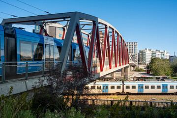 Red steel bridge in Solna Stockholm with tram crossing above railway lines under bright blue sky, showing urban infrastructure, modern connections and public mobility systems