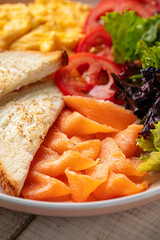 Closeup on healthy breakfast plate with scrambled eggs, toast, smoked salmon and fresh vegetables