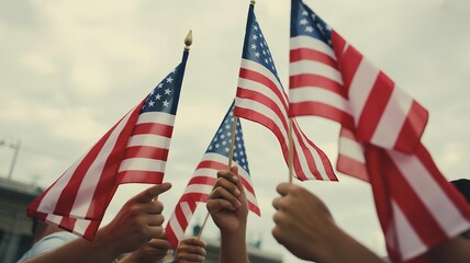 Hands are holding american flags waving against a cloudy sky in a show of patriotism and unity