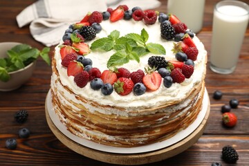 Delicious crepe cake with fresh berries and milk on wooden table, closeup