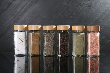 Different spices in glass jars on mirror surface