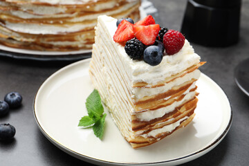 Piece of tasty crepe cake with berries on grey table, closeup