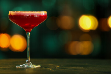 Glass of alcoholic cocktail on table against blurred background. Space for text