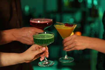 Friends clinking glasses with cocktails in bar, closeup