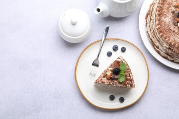Piece of tasty crepe cake with cocoa powder, chocolate, nuts and blackberry served on light table, flat lay. Space for text