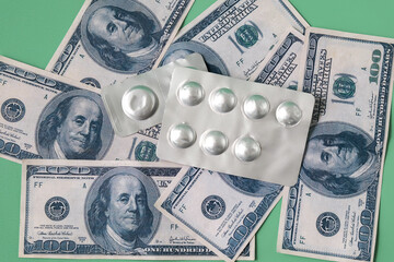 A blister pack of pills and a stack of dollars on a color background.
