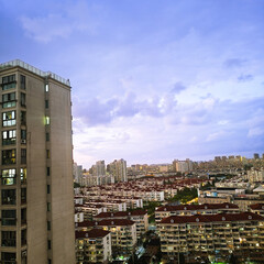 An elevated view of a vast, sprawling city at dusk. In the foreground, dense residential apartment...