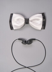 Fototapeta premium Elegant white bow tie and black earbuds on gray background for fashion and music lovers.