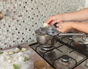 Woman put ravioli into water in pot. 