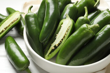Fresh jalapeno peppers in bowl on white wooden table, closeup