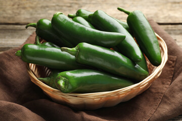Ripe green jalapeno peppers in basket and towel on wooden table, closeup