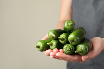 Woman with ripe green jalapeno peppers on light background, closeup. Space for text