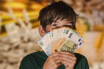 Smiling boy proudly holding a fan of euro banknotes in 20, 50, and 100 denominations, symbolizing wealth, savings, finance, and prosperity.