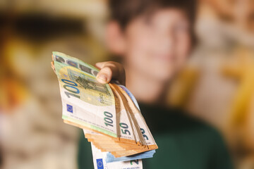 Smiling boy in a green shirt holding fans of 20 and 50 euro banknotes, symbolizing money, savings, wealth, finance, or success.
