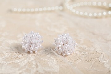 Beautiful pearl earrings and lace fabric on beige background, closeup