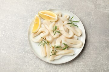 Uncooked squid rings with lemon slices and rosemary on grey table, top view