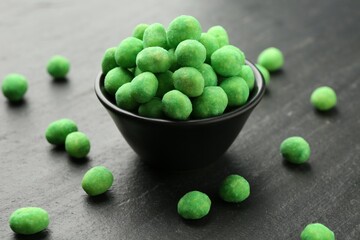 Delicious wasabi coated peanuts and bowl on dark textured table, closeup