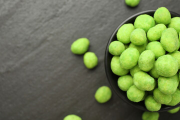 Delicious wasabi coated peanuts and bowl on dark textured table, flat lay. Space for text