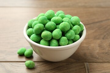 Delicious wasabi coated peanuts in bowl on wooden table, closeup