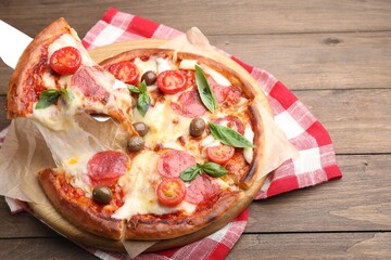 Taking piece of delicious pizza with cheese, salami, tomatoes and olives at wooden table, above view