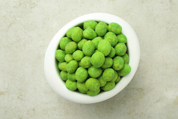 Wasabi coated peanuts in bowl on light table, top view