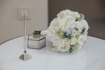 White wedding bouquet on table with ring box and pen