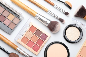Eyeshadow palettes, other cosmetic products and brushes on white background, flat lay