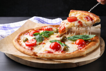 Woman taking piece of delicious pizza with cheese, tomatoes and olives at grey table, closeup