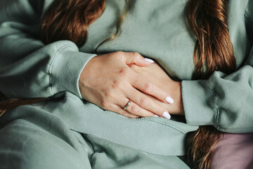 Woman with abdominal pain. Female hands holding stomach. Menstrual cramps symptom closeup. Woman in...