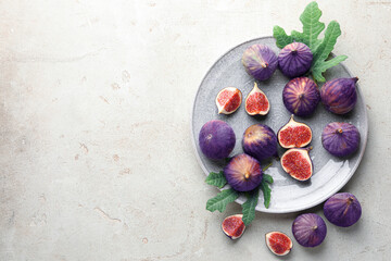 Fresh ripe figs and green leaves on gray textured table, flat lay. Space for text