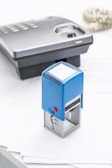 Office secretary uses a blue stamp next to a telephone and paperwork on a busy desk during a workday
