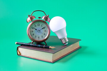 Alarm clock ,Light bulb with Fountain pen on old book background.Education concept.