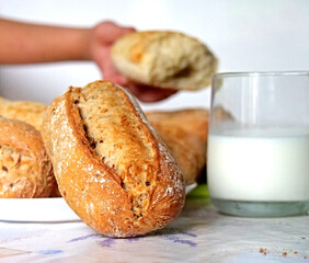 Naklejka premium A Hand Breaking Open a Fresh, Crusty Bread Roll Next to a Glass of Milk