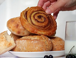 Hand taking a cinnamon bun from a plate - A Person Choosing a Sweet Pastry from a Breakfast Spread