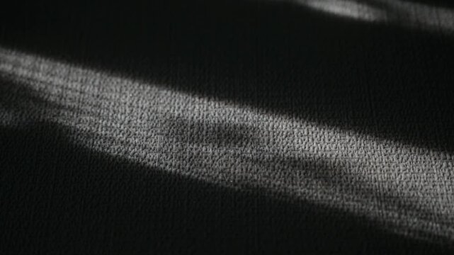 Abstract Light and Shadow on Dark Textile. Close up view of parallel streaks of light illuminating a dark gray textured fabric. 