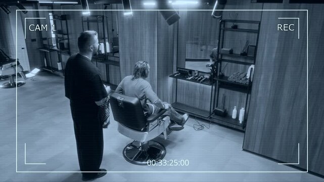 Full overhead CCTV shot of young Caucasian barber and male client with wet hair walking over to chair, sitting down, putting cape on shoulders, before discussing haircut request