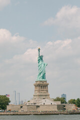 Fototapeta premium Statue of Liberty stands tall in New York Harbor on a clear day with clouds in the background