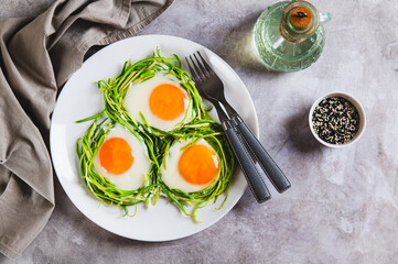 Appetizing zucchini noodle nests with fried eggs on a plate on the table top view