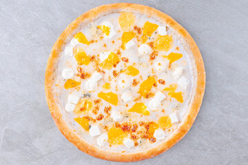 Top view of gourmet cheese pizza with peach slices and creamy sauce on gray background. Creative sweet and savory pizza concept